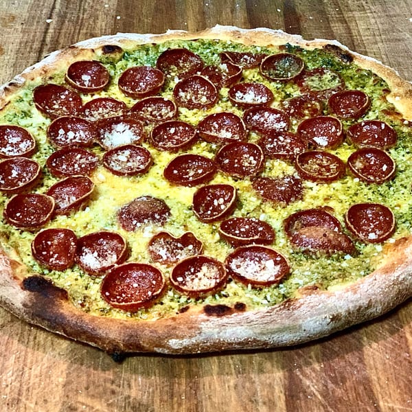 GOOMAH's pepperoni pizza, with pesto and cheese, on a wooden surface.