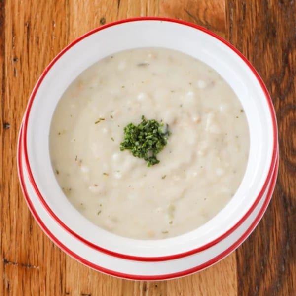 Creamy white soup with green herbs in a white bowl with red trim on a wooden table.