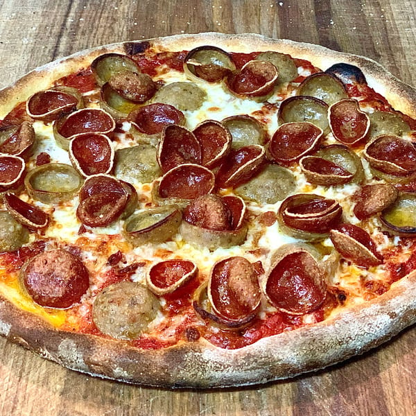 GOOMAH's Italian pizza with pepperoni, sausage, melted cheese, and tomato sauce on a wooden surface.