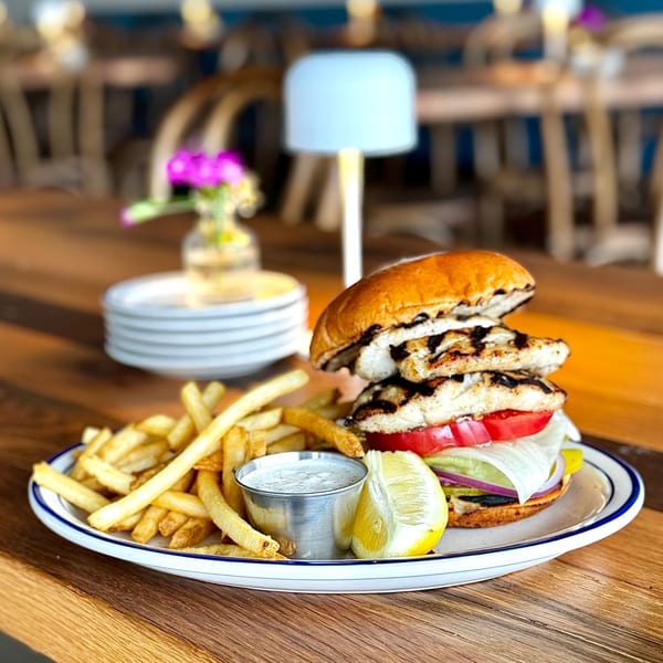 Grilled chicken sandwich with fries, lemon, and dipping sauce on a white plate at GOOMAH.