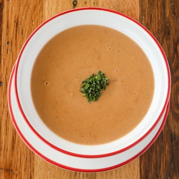 Creamy Italian soup with a garnish of chopped chives in a white bowl with red rim.