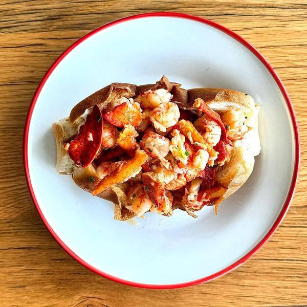 A lobster roll with generous chunks of lobster meat and claws on a white plate with a red rim.