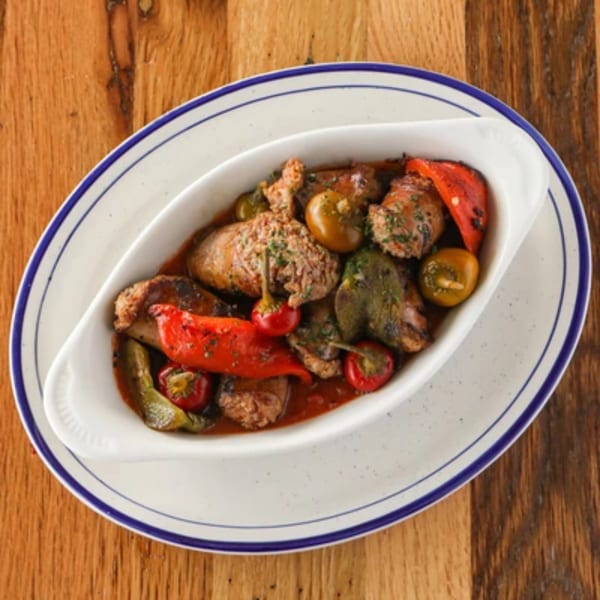 Italian sausage and peppers in a white oval dish with blue rim on a wooden table.