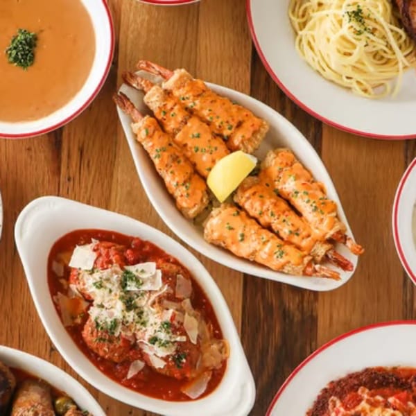 Overhead view of Italian dishes including soup, shrimp, spaghetti, and meatballs on a wooden table.