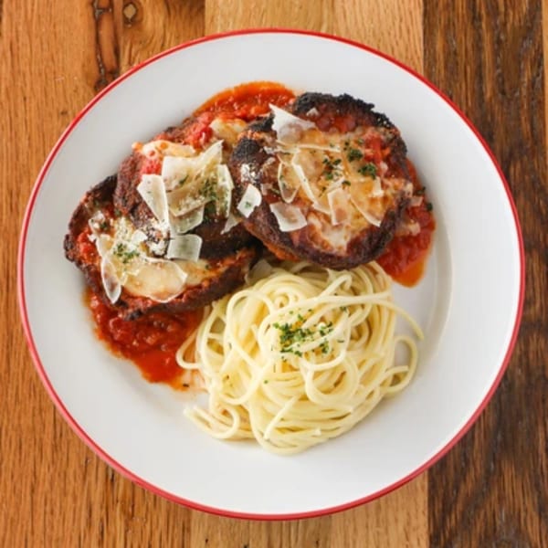 Italian dish with two breaded cutlets in red sauce, topped with cheese, beside a pile of spaghetti.
