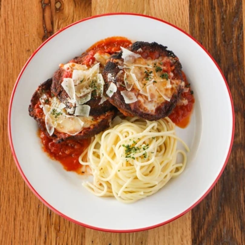 Italian dish with two breaded cutlets in red sauce, topped with cheese, beside a pile of spaghetti.