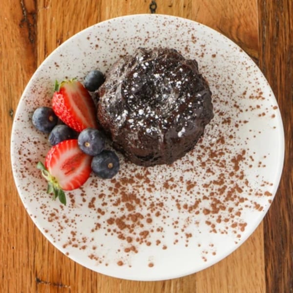 Chocolate lava cake with powdered sugar, fresh strawberries, and blueberries on a white plate.