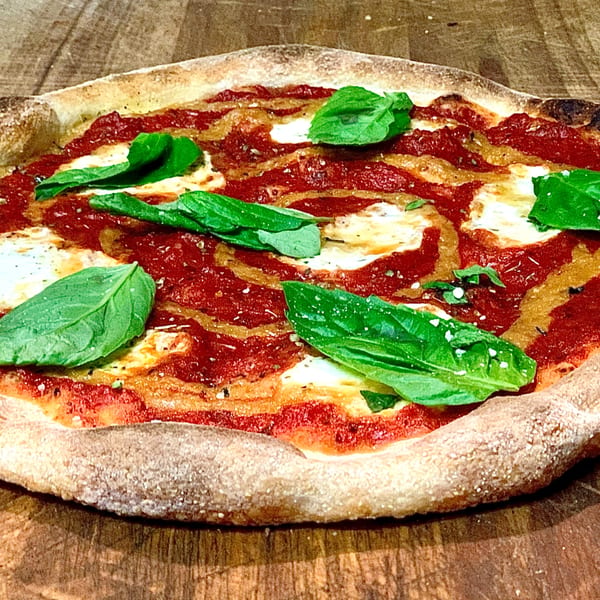 A GOOMAH Margherita pizza with fresh basil leaves, tomato sauce, and mozzarella cheese.