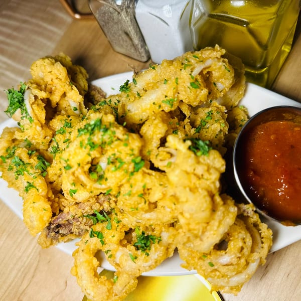 Crispy fried calamari with fresh parsley and a side of marinara sauce on a white plate.