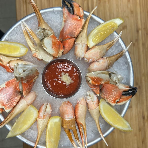 Stone crab claws and lemon wedges arranged around a bowl of cocktail sauce on ice.