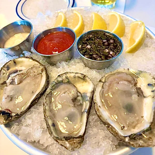 Three fresh oysters on ice with lemon wedges and three dipping sauces at GOOMAH.