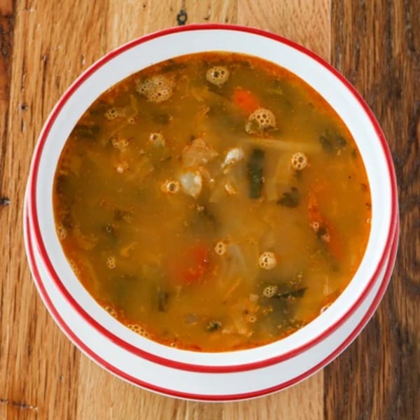 Hearty Italian vegetable soup with carrots and greens in a white bowl with red stripes.