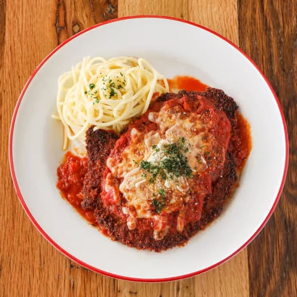 Chicken parmesan with spaghetti and red sauce, garnished with parsley on a white plate.