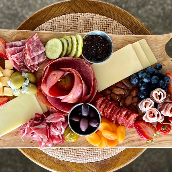 A wooden charcuterie board with Italian meats, cheeses, olives, fruits, nuts, and pickles.