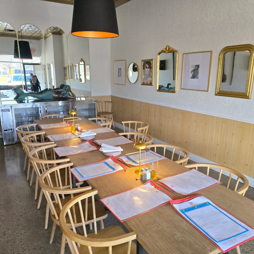 Long wooden dining table set with menus and chairs in a bright Italian restaurant.