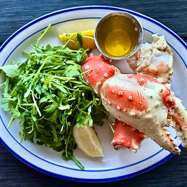 King crab legs with arugula, lemon wedges, and a side of melted butter on a white plate.