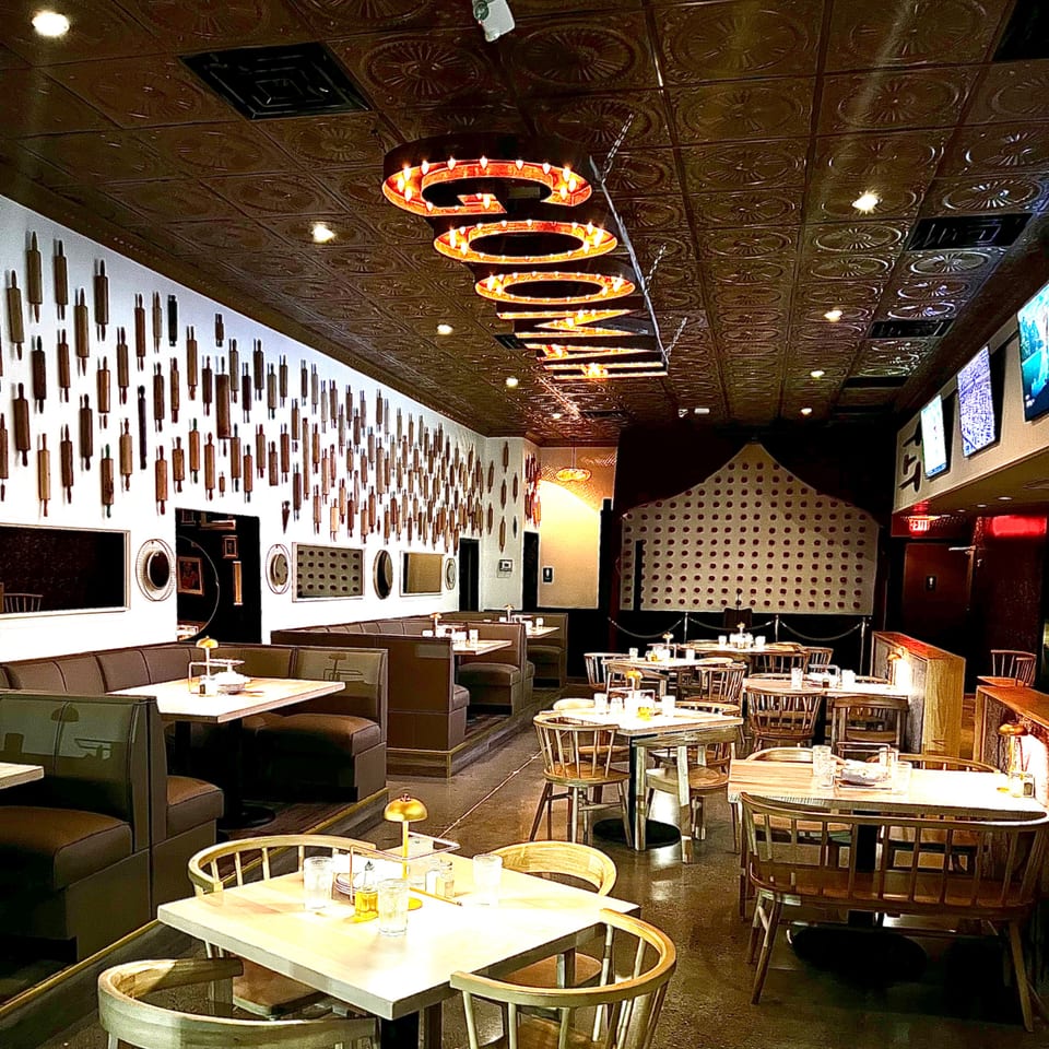 Interior of GOOMAH restaurant with booth seating, wooden tables, and a wall decorated with rolling pins.