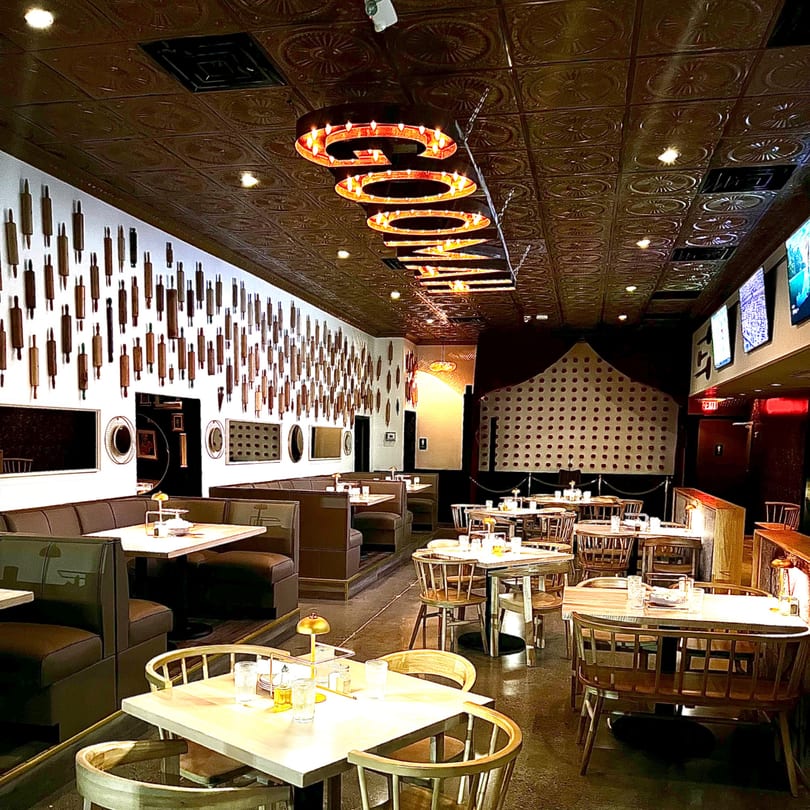 Interior of GOOMAH restaurant with booth seating, wooden tables, and a wall decorated with rolling pins.