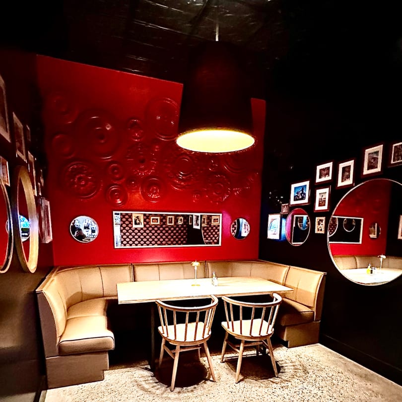 A cozy Italian restaurant interior with a red accent wall, booth seating, and wooden chairs.