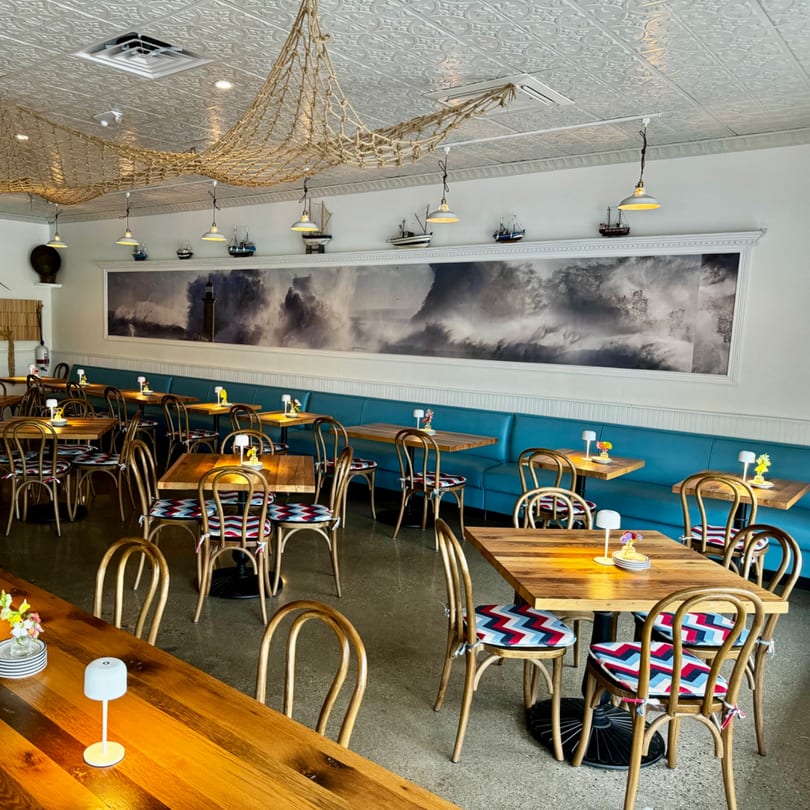 GOOMAH restaurant interior with wooden tables, blue banquettes, nautical decor, and a large wave mural.
