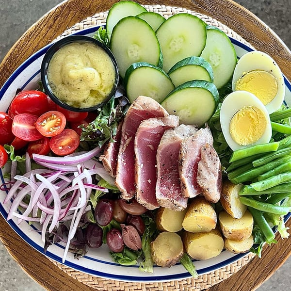 A vibrant Italian Niçoise salad with seared tuna, eggs, green beans, potatoes, olives, and dressing.
