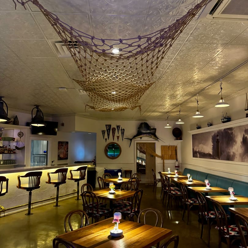 The GOOMAH Italian restaurant interior features a bar, dining tables, and nautical decor with fishing nets.