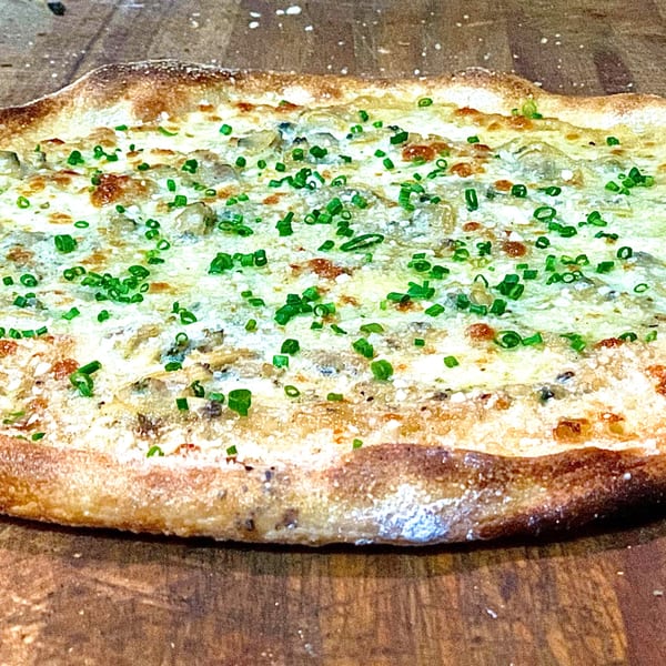 GOOMAH's white pizza with melted cheese, mushrooms, and fresh green chives on a wooden surface.