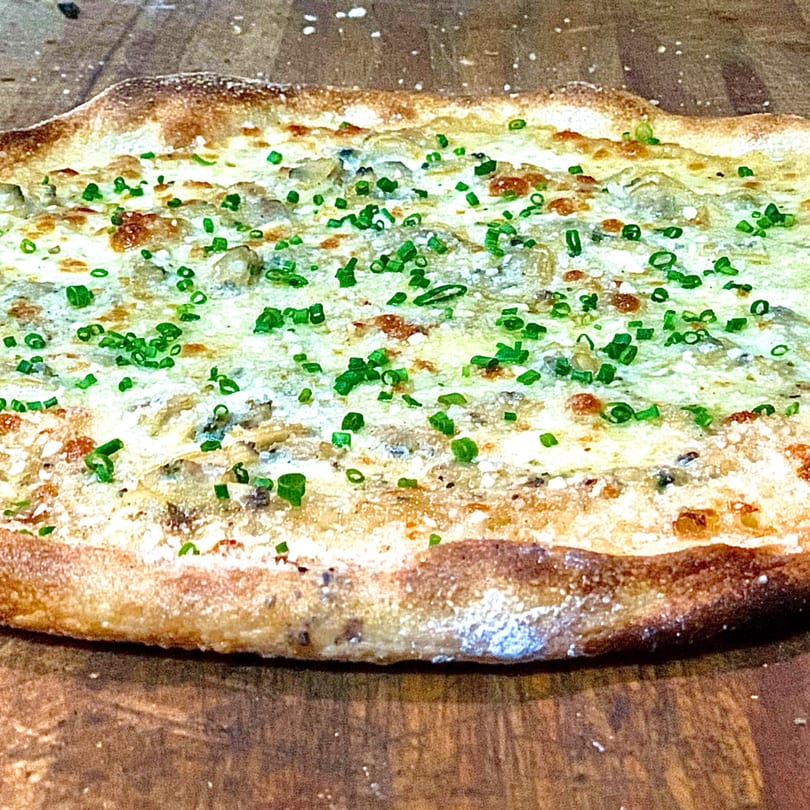 GOOMAH's white pizza with melted cheese, mushrooms, and fresh green chives on a wooden surface.