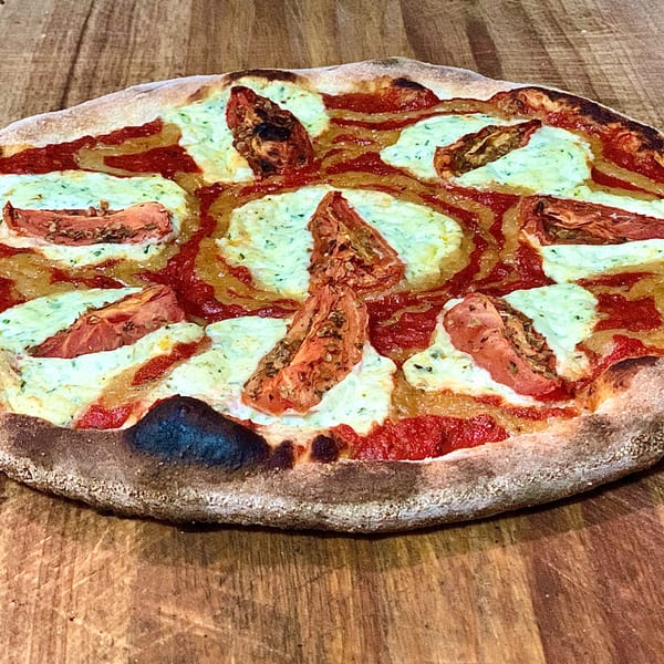 GOOMAH's Italian pizza with red sauce, white cheese, and sun-dried tomatoes on a wooden surface.