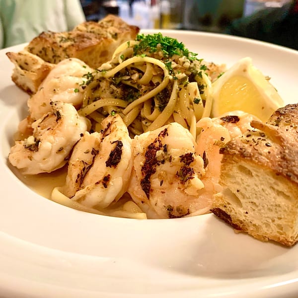 GOOMAH's shrimp scampi with linguine, garlic bread, and a lemon wedge on a white plate.