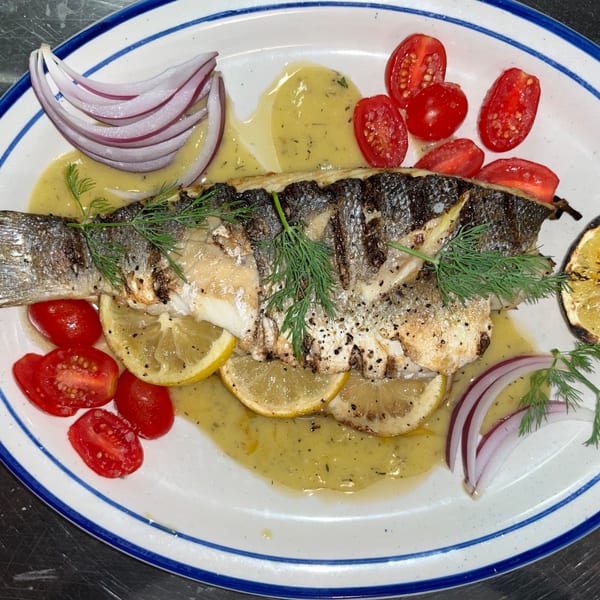 Whole grilled fish with lemon slices, cherry tomatoes, red onion, and dill on a white plate.